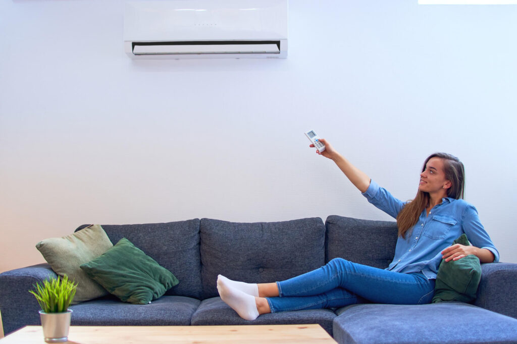 young happy woman sitting couch air conditioner adjusting comfort temperature with remote control modern home